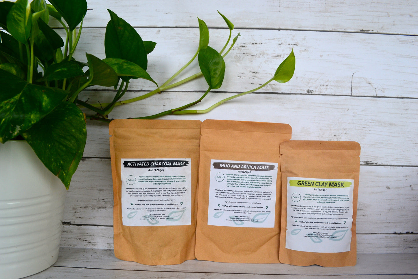 Three brown paper bags with skincare mask labels on a wooden surface with a plant in the background.