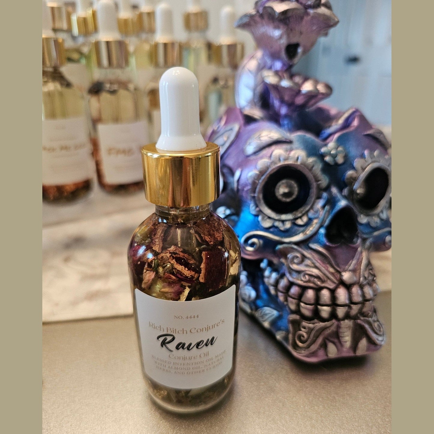 Bottle of 'Raven' with a dropper labeled 'Rich Bitch Conjure' next to a decorative skull. Raven Hoodoo Conjure Oil for Intuition, Manifestation, & Spiritual Power Ritual Oil