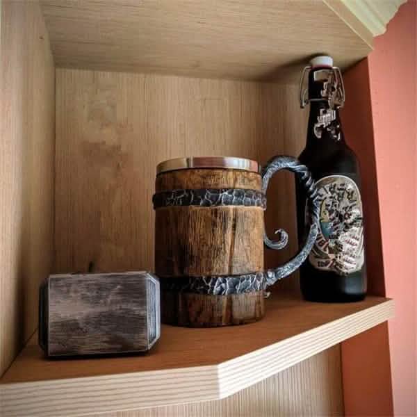 Wooden barrel-shaped mug with decorative handle on a shelf next to a bottle.