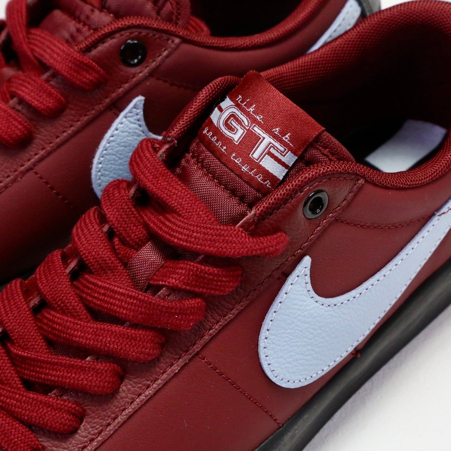 Close-up of a Nike sneaker in deep red with a white Swoosh, matching red laces, and a red tongue label featuring white text. Nike SB Blazer Low Pro GT DV1226-600