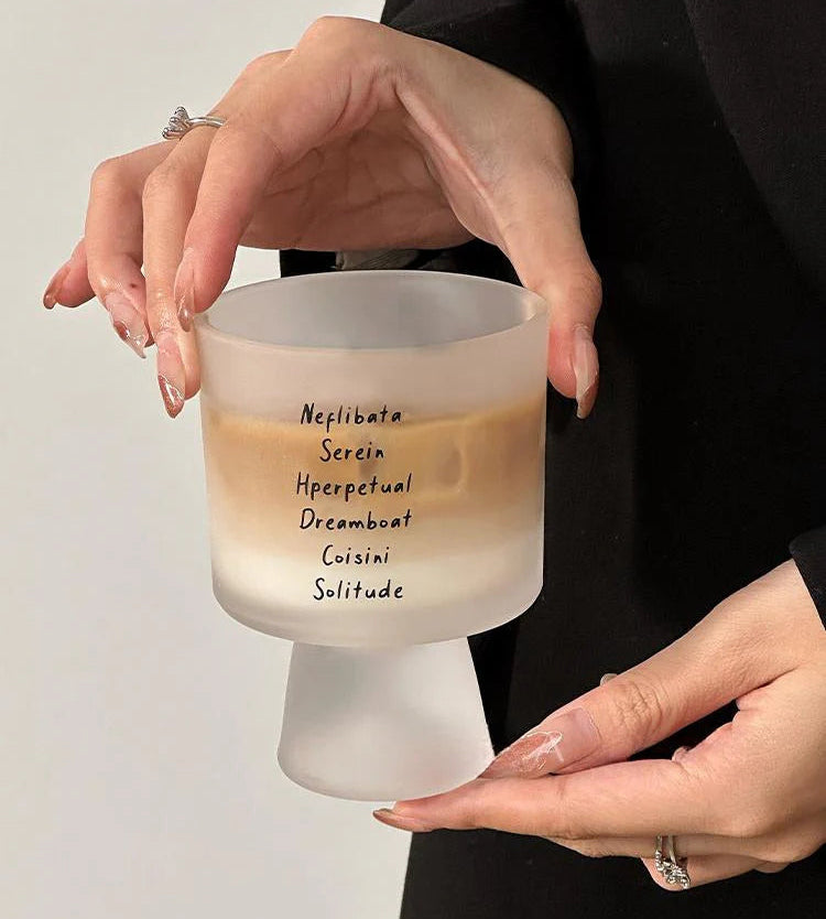 Frosted glass candle with text held by a person against a neutral background