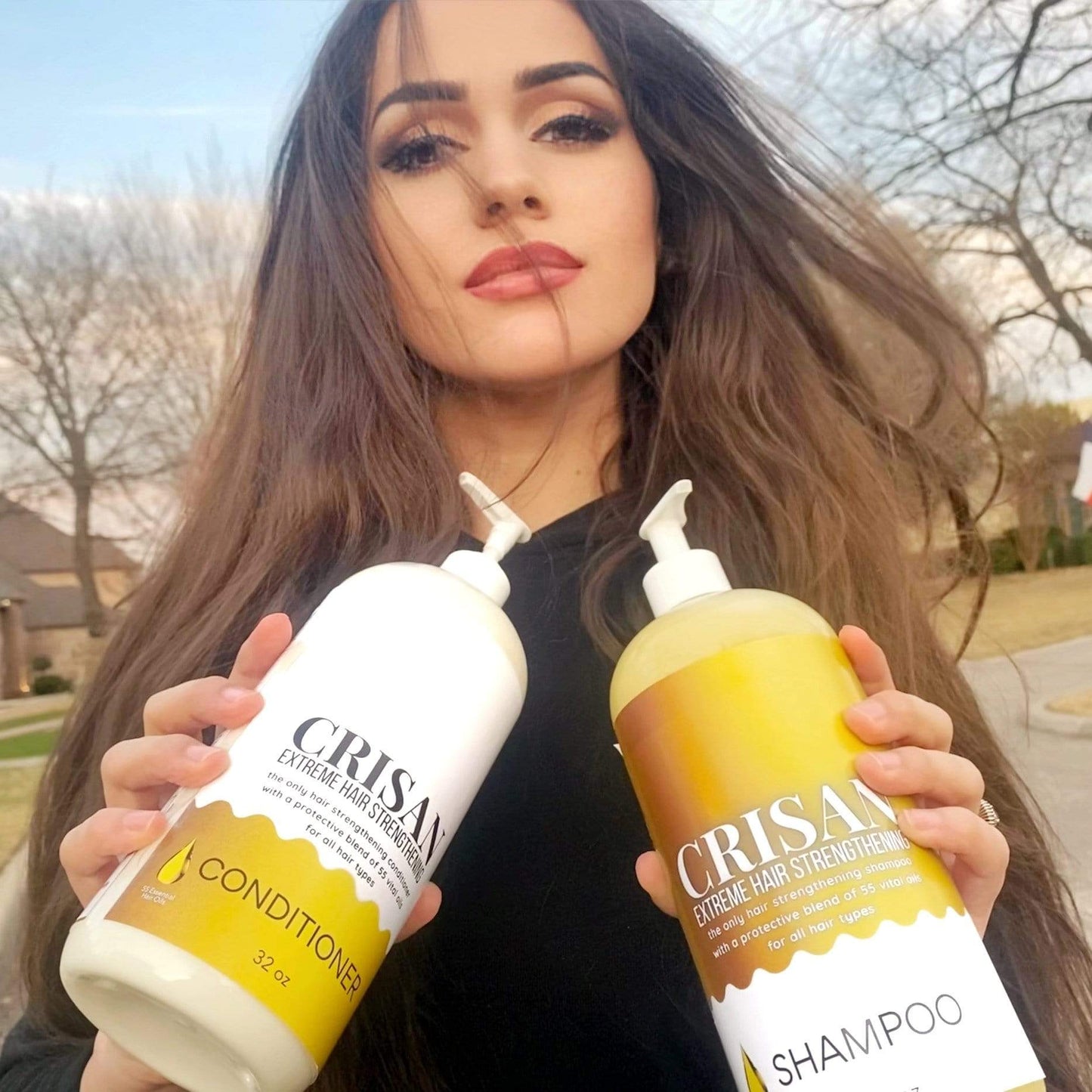 Woman holding two bottles of Crisan shampoo and conditioner outdoors.