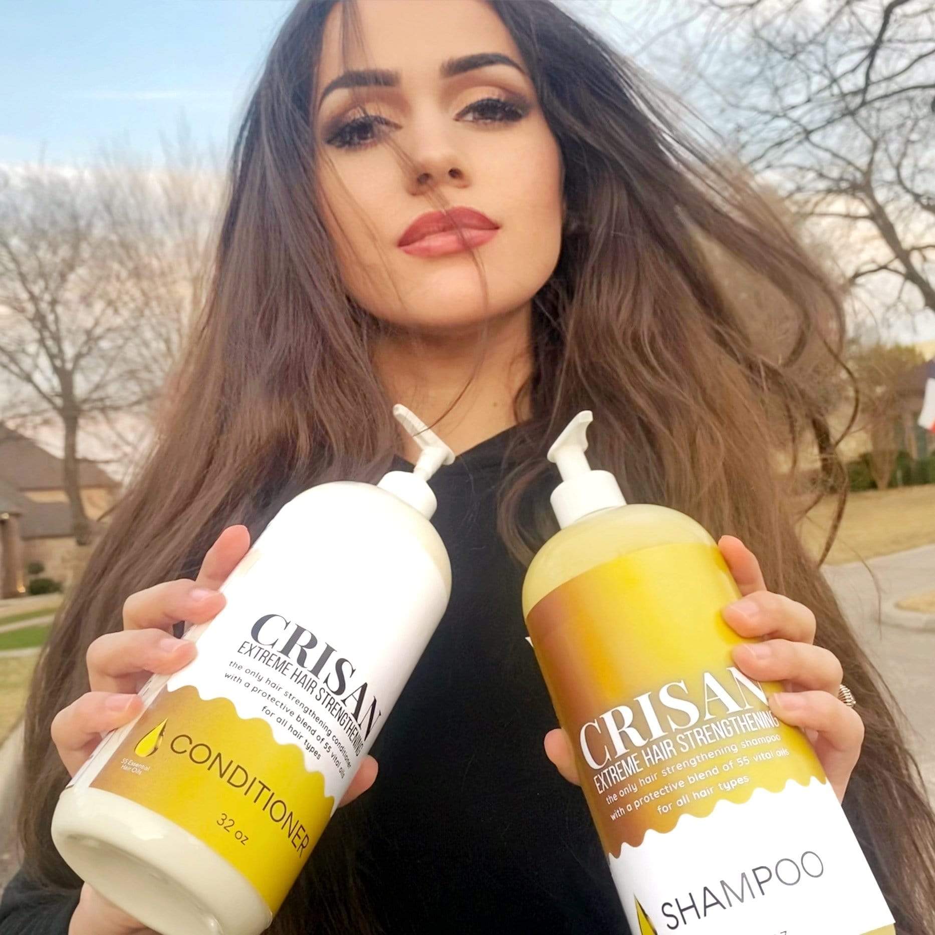 Woman holding two bottles of Crisan shampoo and conditioner outdoors.