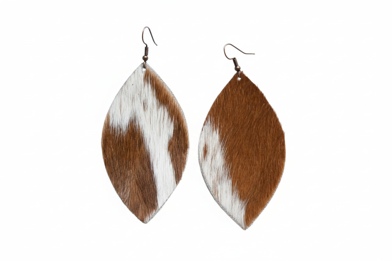 Pair of leaf-shaped earrings with brown and white pattern on a light wooden surface