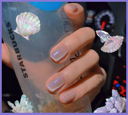 Hand holding a Starbucks cup with shell designs and iridescent nail polish.