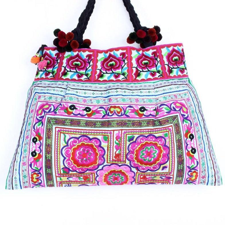 Handcrafted boho-style tote bag from Thailand, featuring colorful traditional embroidery, soft cotton lining, and playful pompom fringe detailing, displayed on a neutral background.