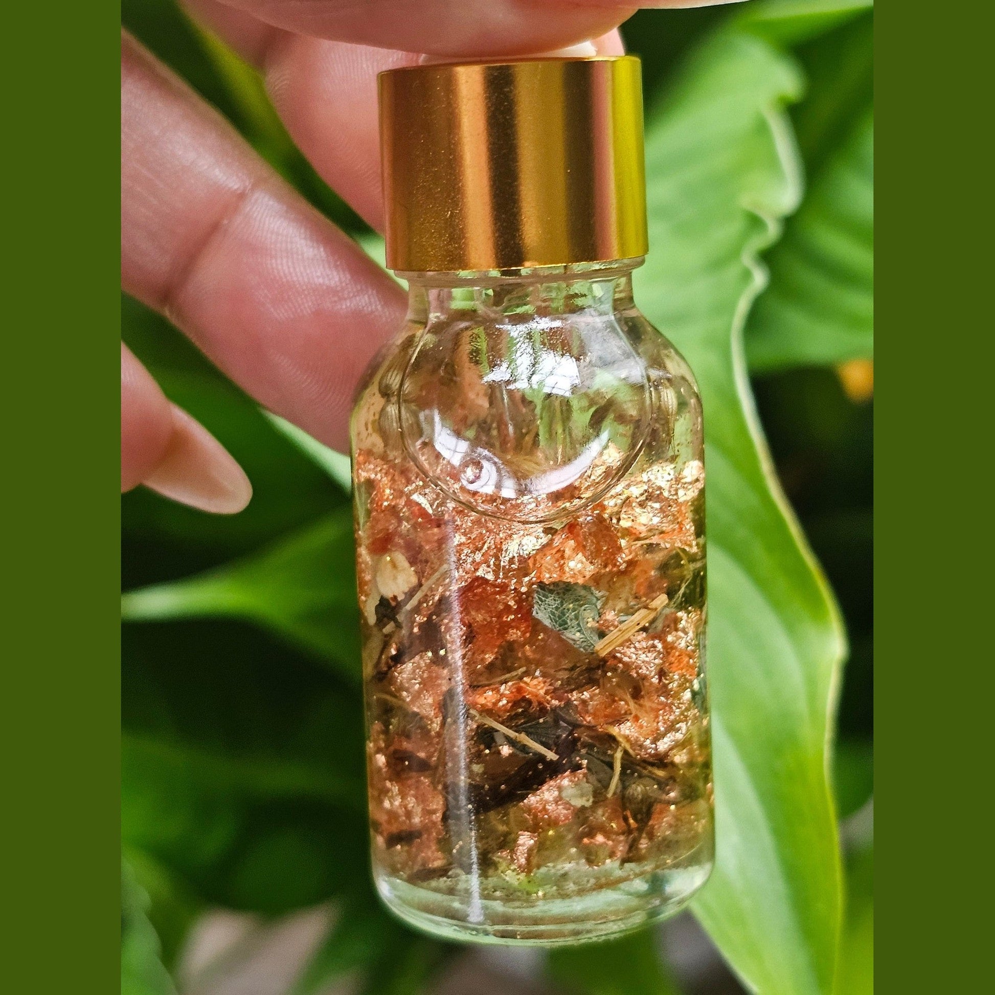 Small glass bottle with a gold cap containing a mixture of herbs and liquids, held against a green leafy background. Lucky Girl Sweetening Hoodoo Conjure Oil | Good Luck Oil | Favor and Opportunity Oil | Prosperity Ritual Oil | Rootwork Spiritual Supply
