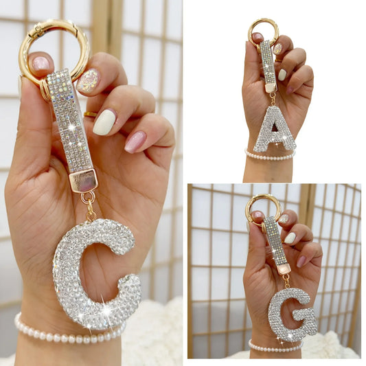 Sparkling rhinestone letter **C** keychain with a gold-tone round key ring and crystal-studded strap, held in a hand and shown from multiple angles against a softly blurred indoor background.
