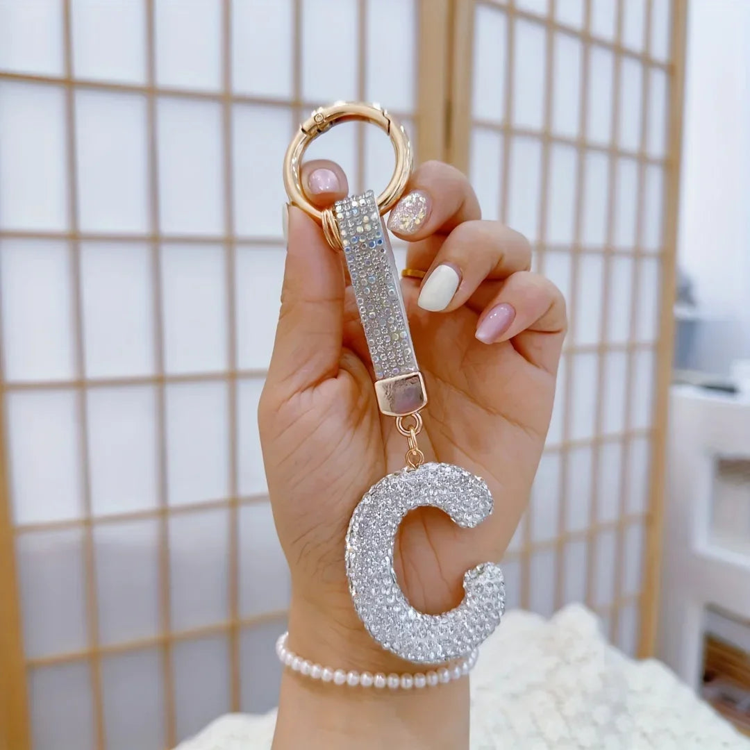 Sparkling rhinestone letter C keychain with a gold-tone key ring and crystal-covered initial charm, shown held in hand against a soft neutral background. Decorative alphabet pendant for keys, handbags, backpacks, or gifts.
