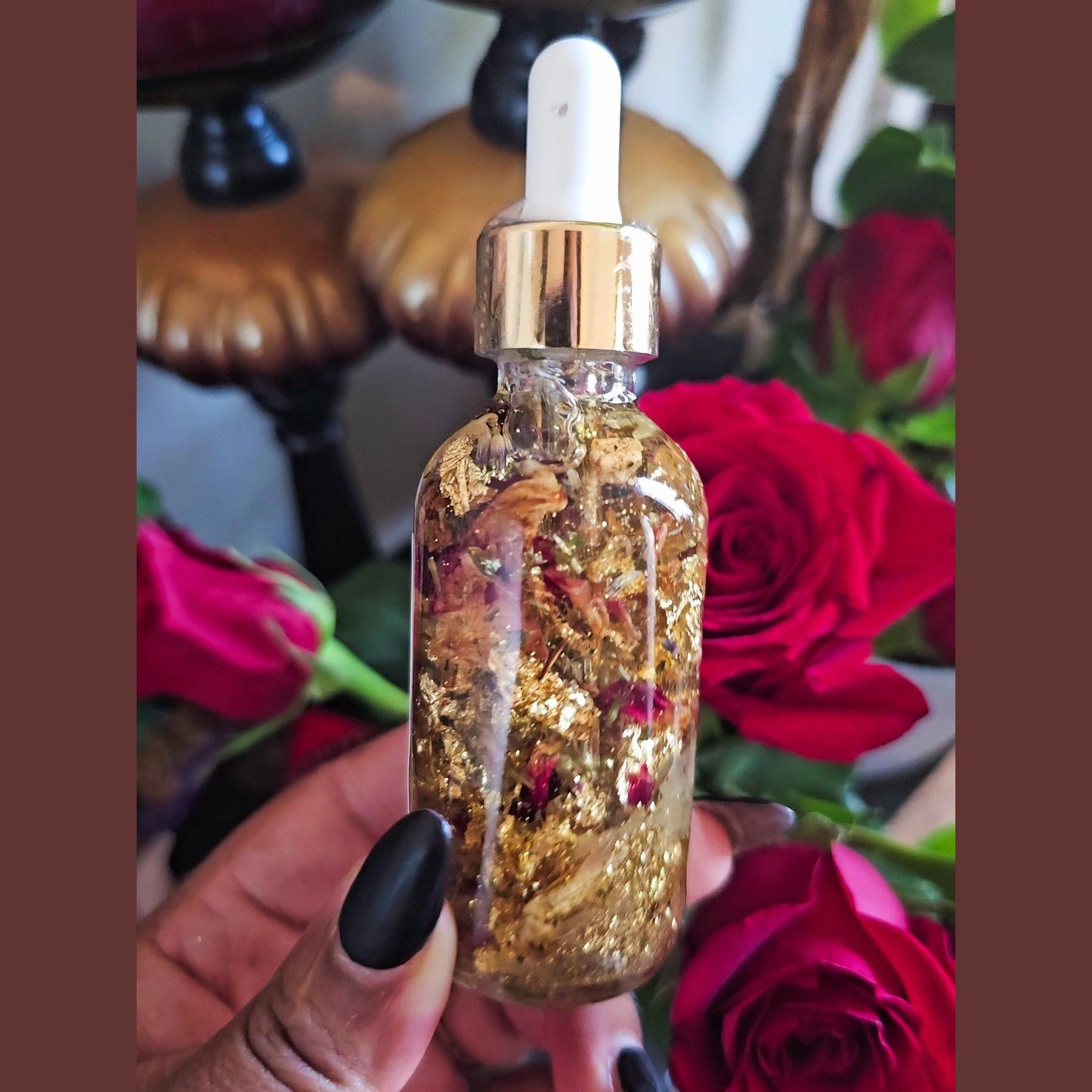 Bottle with gold liquid and dropper held in front of red roses. Lucky Rich Girl Hoodoo Conjure Oil | Wealth, Beauty, Glamour & Good Fortune Conjure Oil | Limited Edition
