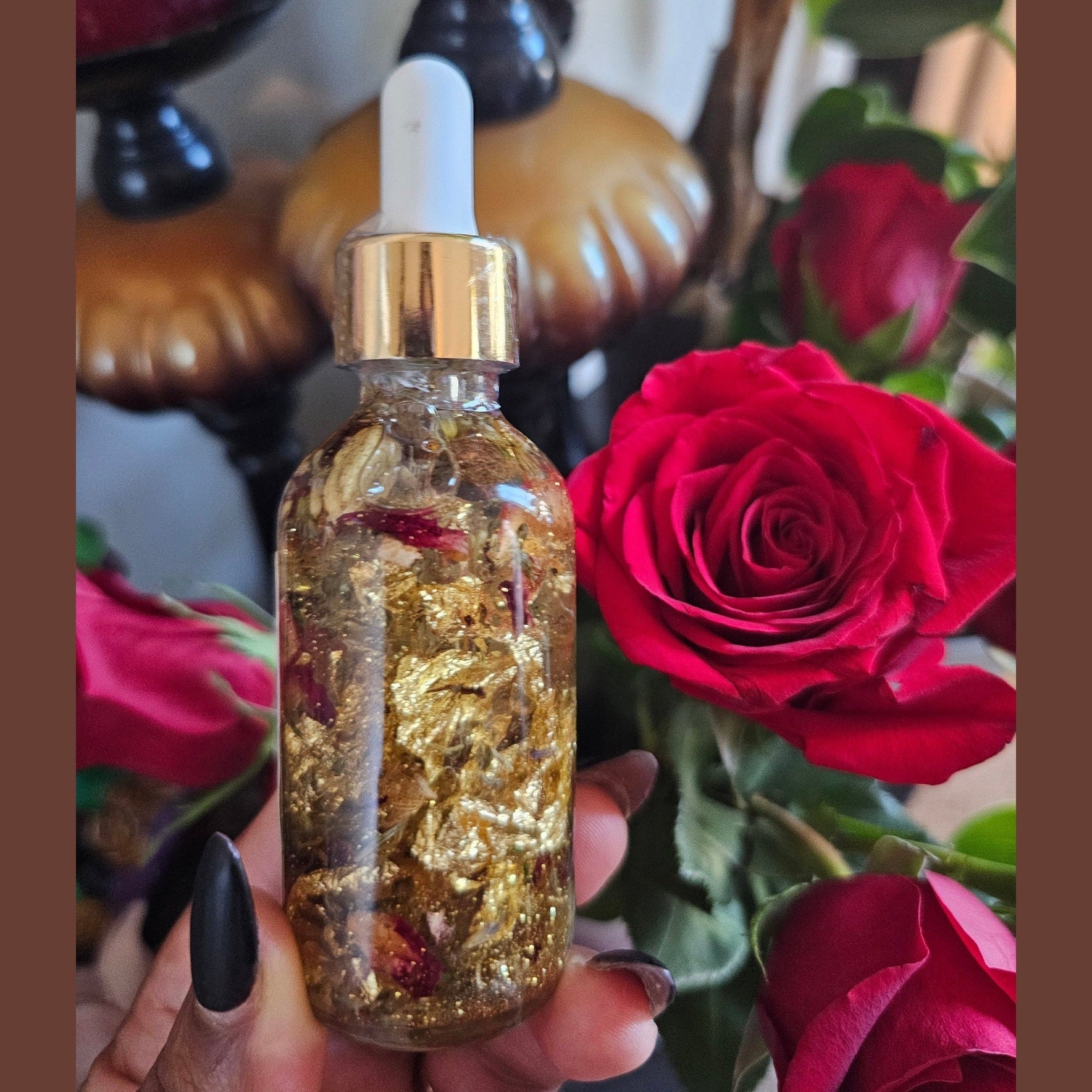 Bottle with gold contents held in front of red roses. Lucky Rich Girl Hoodoo Conjure Oil | Wealth, Beauty, Glamour & Good Fortune Conjure Oil | Limited Edition