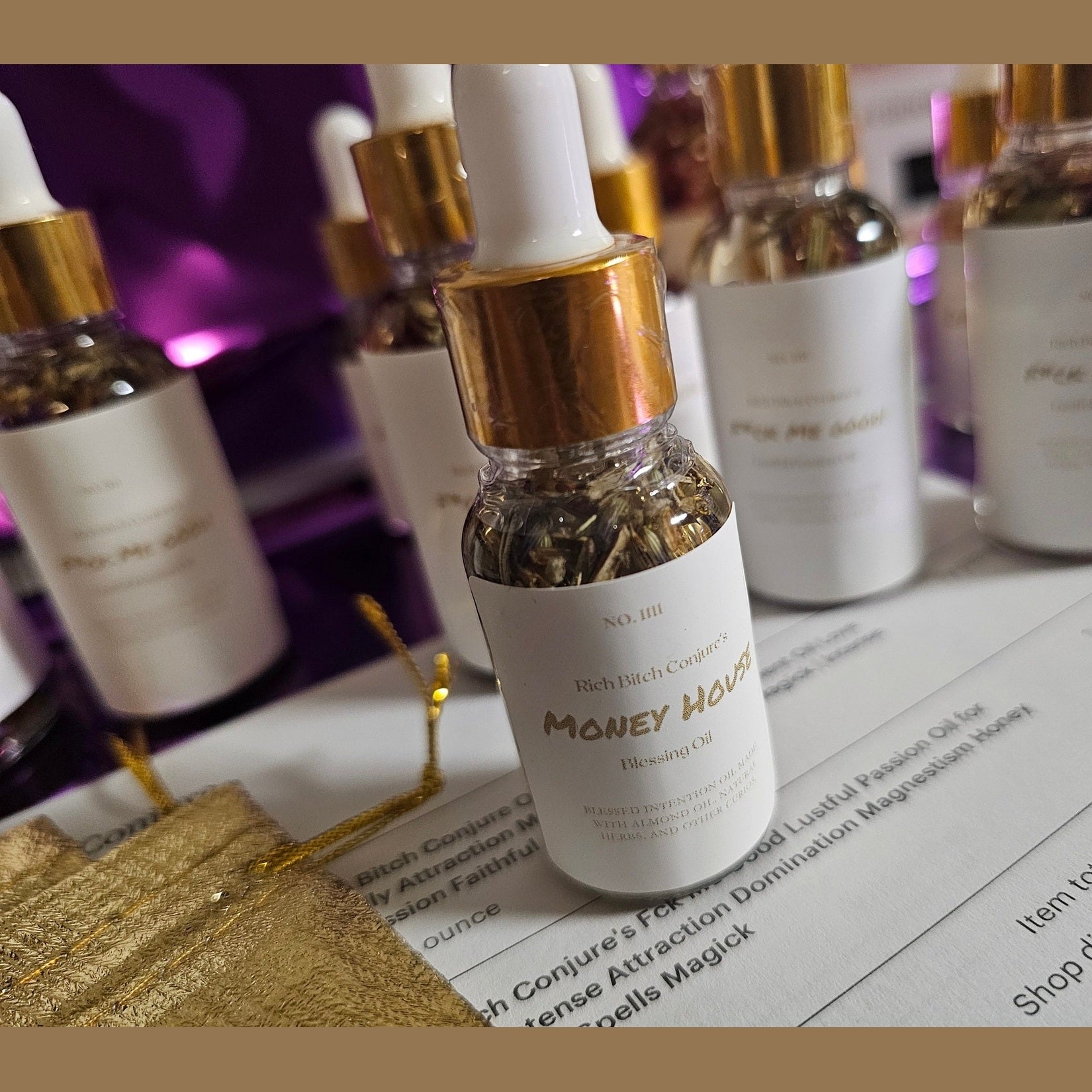 Bottle of 'Money Mojo' oil with gold cap on a table with other similar bottles. Rich Bitch Conjure's Money House Blessing Oil