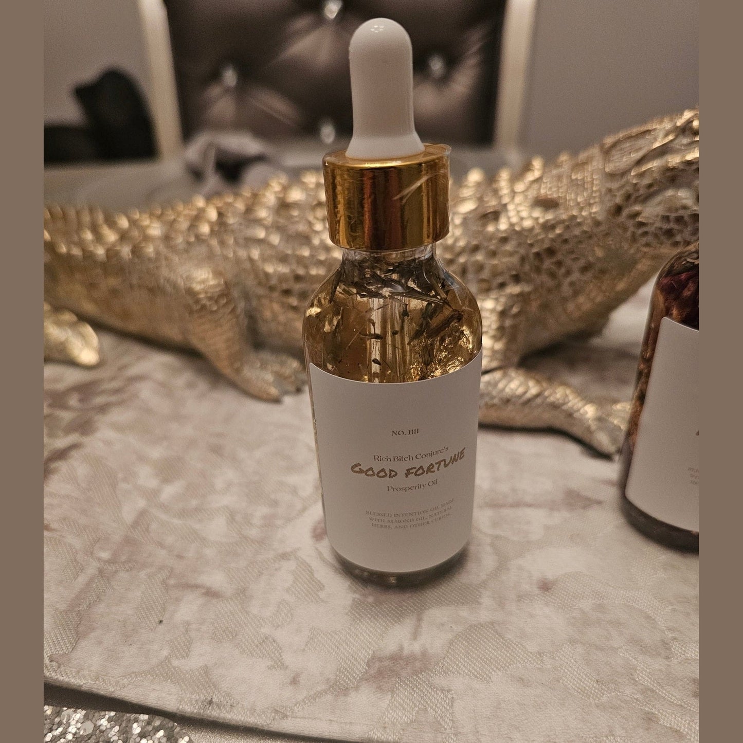 Gold bottle with dropper on a decorative surface. Rich Bitch Conjure's Good Fortune Oil