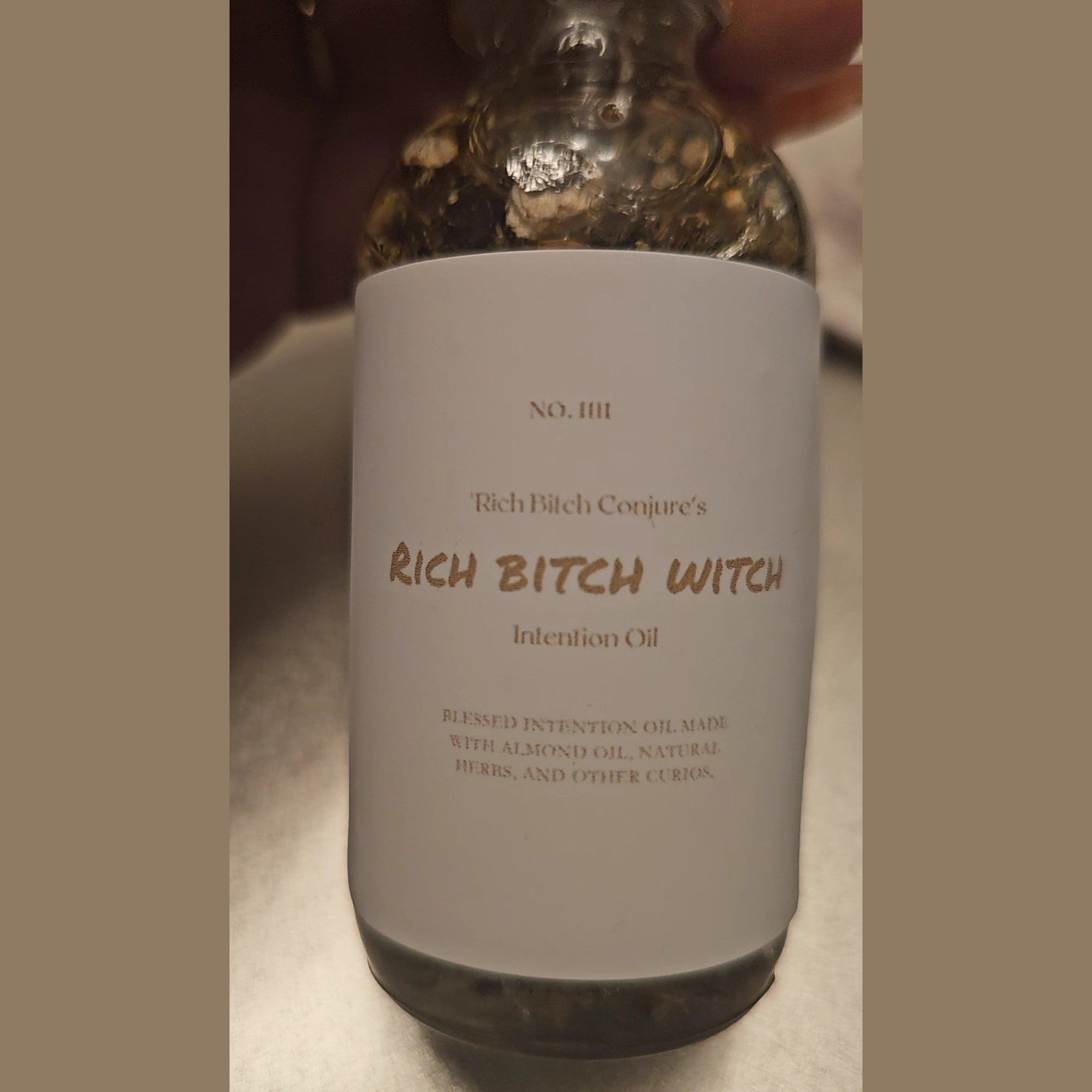 Bottle labeled 'Rich Bitch Conjure's Rich Bitch Witch Intention Oil' held by a hand. Rich Bitch Conjure's Rich Witch Bitch Intuitive Oil