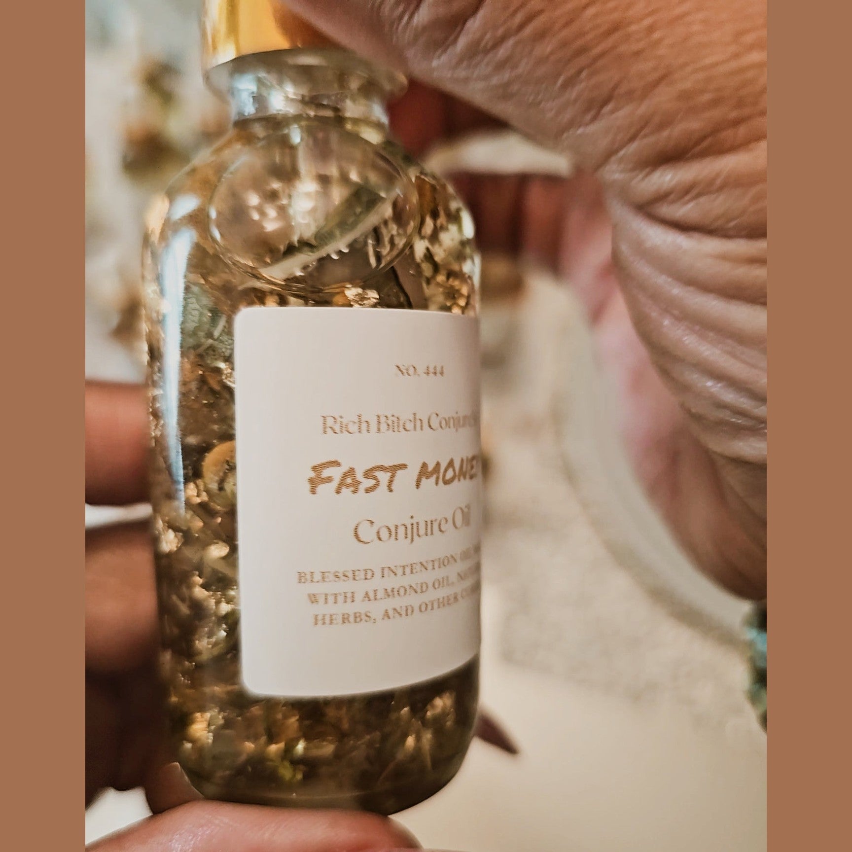 Hand holding a small glass bottle labeled 'Fast Money Conjure Oil' with a blurred background. Fast Money Oil - Luxury Hoodoo Conjure Oil for Quick Cash & Prosperity