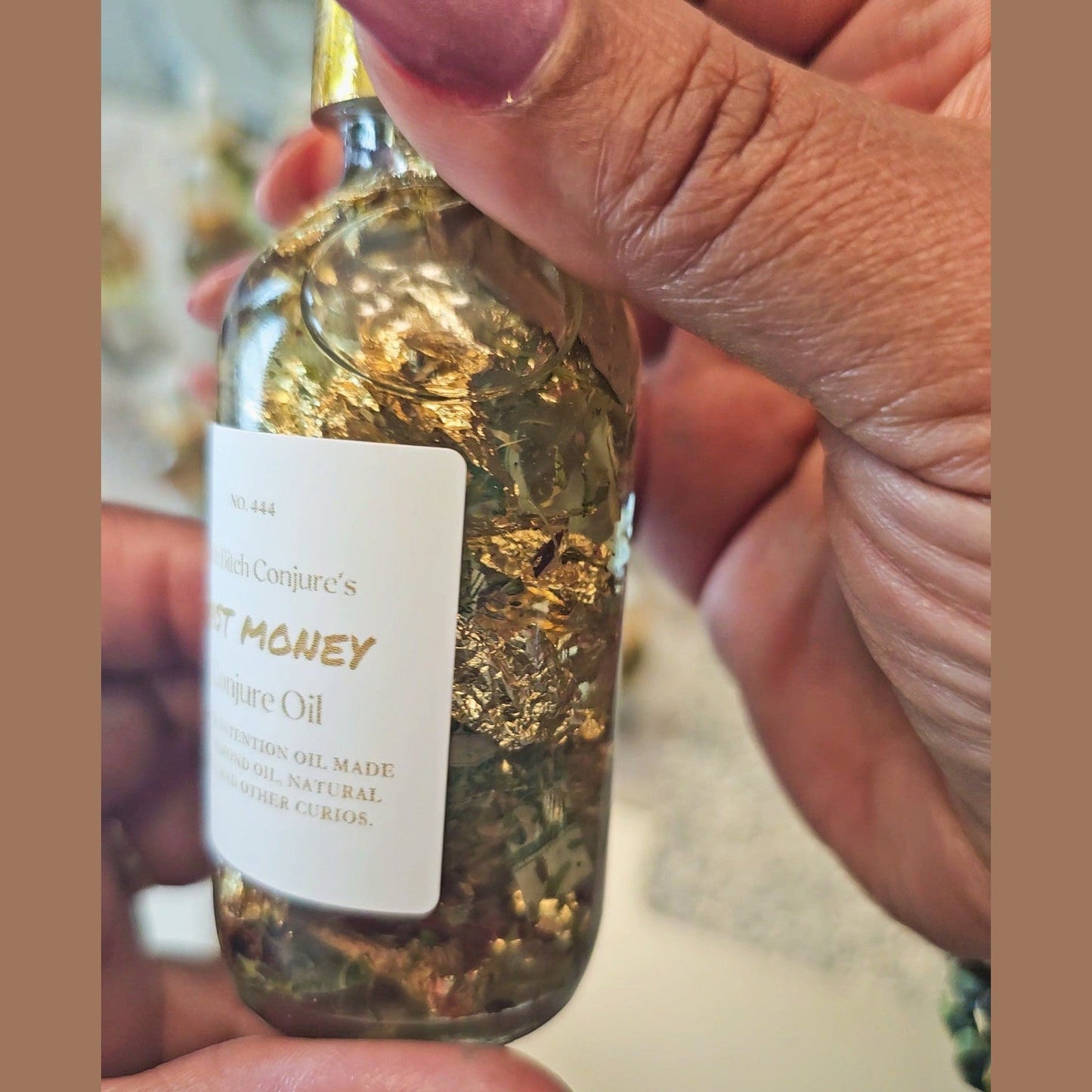 Hand holding a small bottle labeled 'Best Money Cure Oil' with gold flakes. Fast Money Oil - Luxury Hoodoo Conjure Oil for Quick Cash & Prosperity
