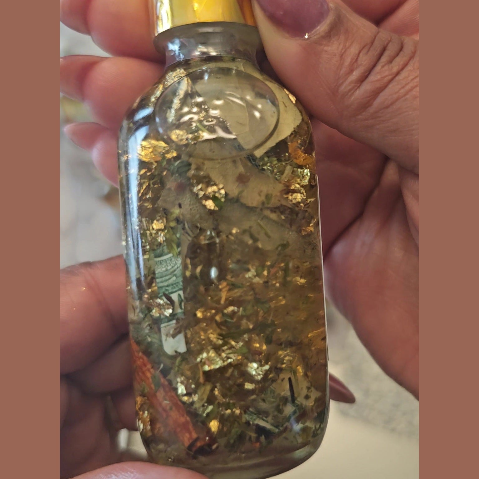 Glass bottle with gold leaf held by a hand.  Fast Money Oil - Luxury Hoodoo Conjure Oil for Quick Cash & Prosperity