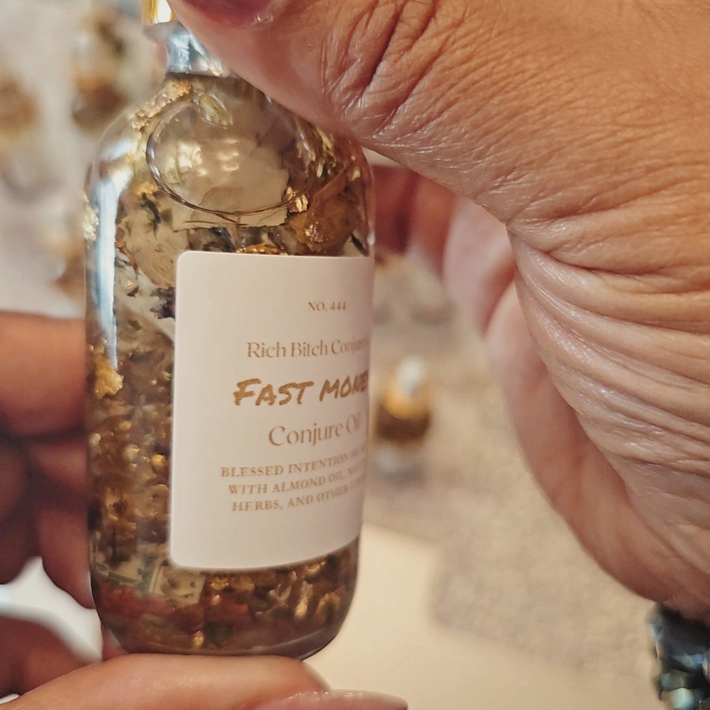 Hand holding a small glass bottle labeled 'Fast Mode Conjure Oil' with a blurred background. Fast Money Oil - Luxury Hoodoo Conjure Oil for Quick Cash & Prosperity