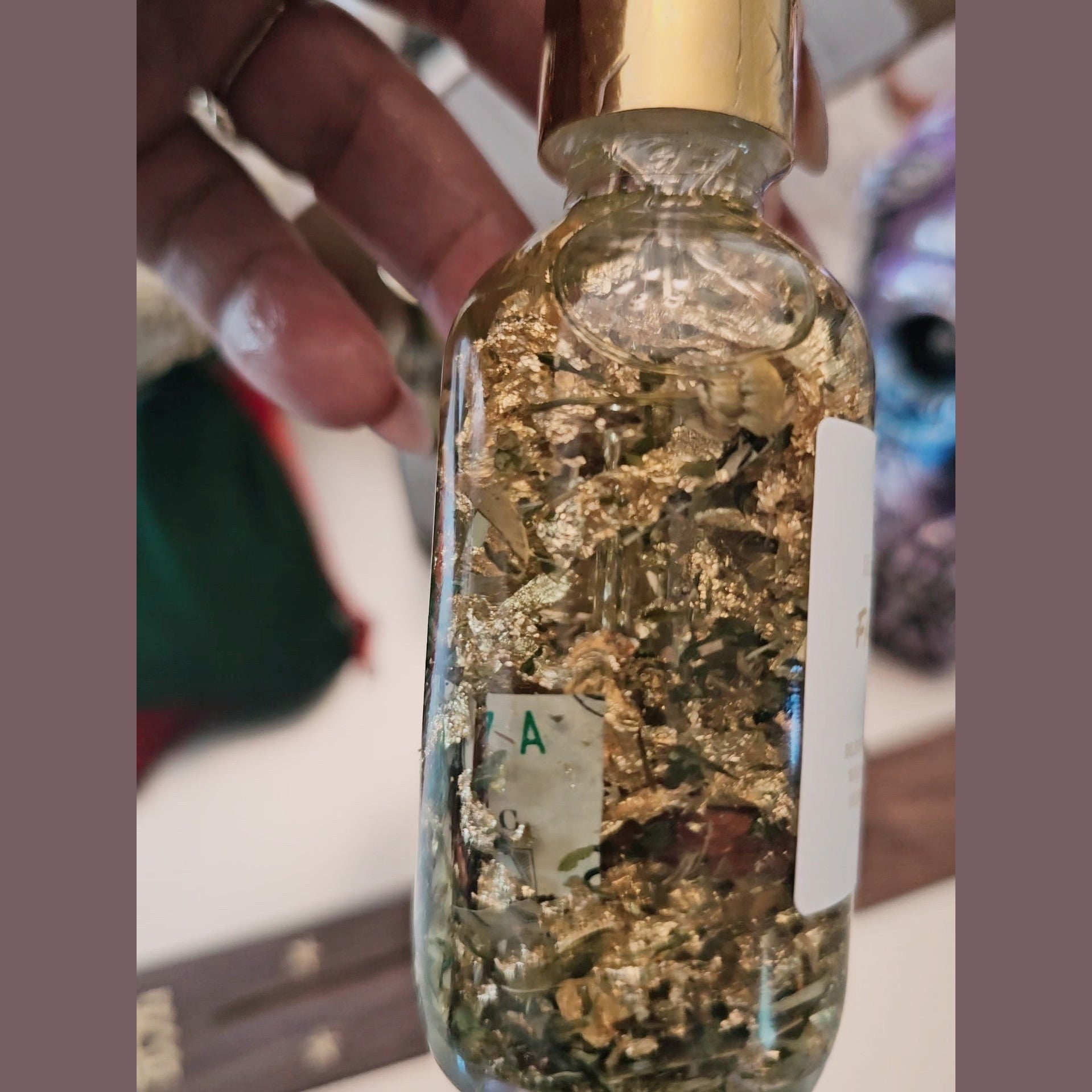 Glass bottle filled with gold flakes held by a hand. Fast Money Oil - Luxury Hoodoo Conjure Oil for Quick Cash & Prosperity