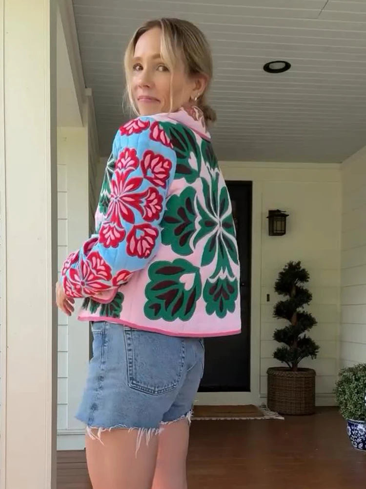 Woman wearing a colorful floral jacket and denim shorts standing in a doorway.