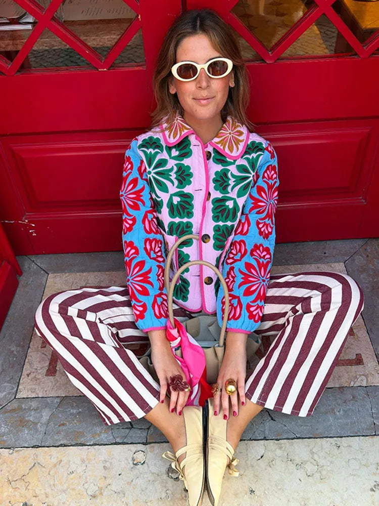 Woman in colorful floral jacket and striped pants sitting on a red door step.