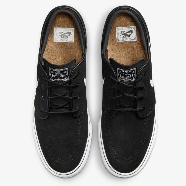 A pair of Nike SB Jack 1 low-top sneakers in black suede and canvas, featuring white rubber soles and white Swoosh logos on the sides, photographed from a top-down angle on a light gray background. Nike SB Janoski Black White
