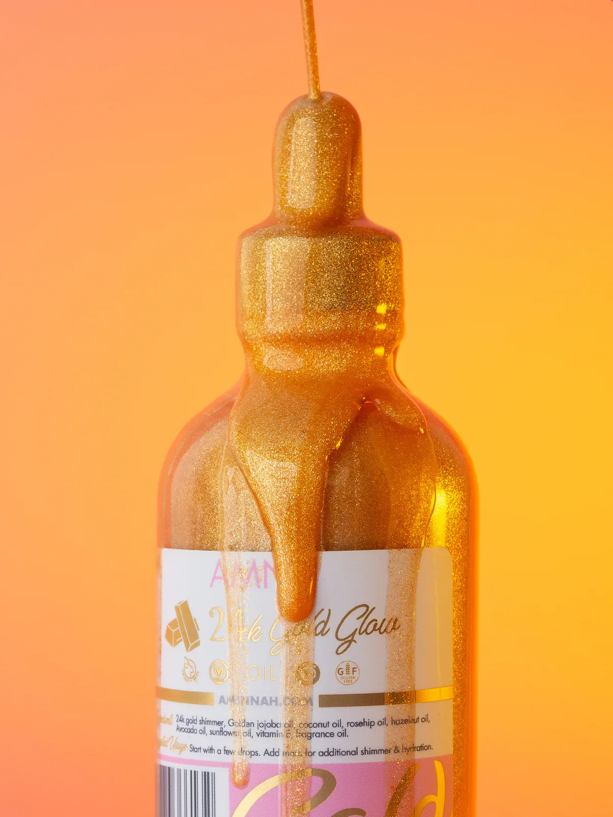 24K Gold Glow Body Oil bottle with shimmering gold oil dripping from the dropper against a warm golden background, hydrating body shimmer oil for radiant glowing skin.