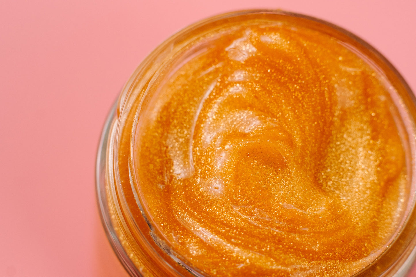 Close-up of a jar of orange glittery substance on a pink background. 24K Gold Jelly Face Mask – Hydrating Aloe Vera, Rose Extract & Vitamin E | Vegan Skincare