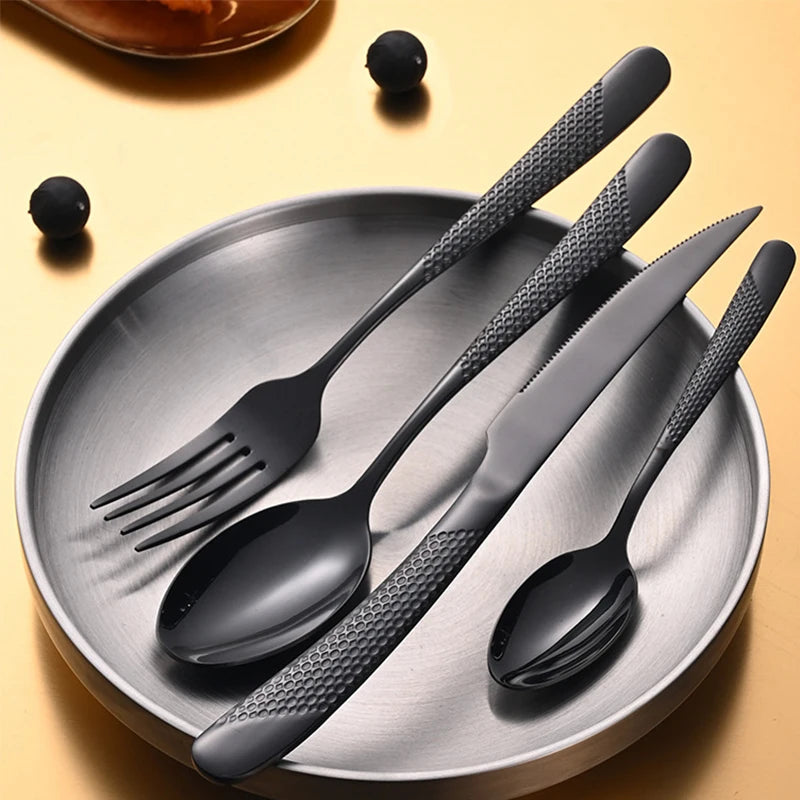 Set of black cutlery including fork, spoon, and knife on a gray plate with a yellow background.