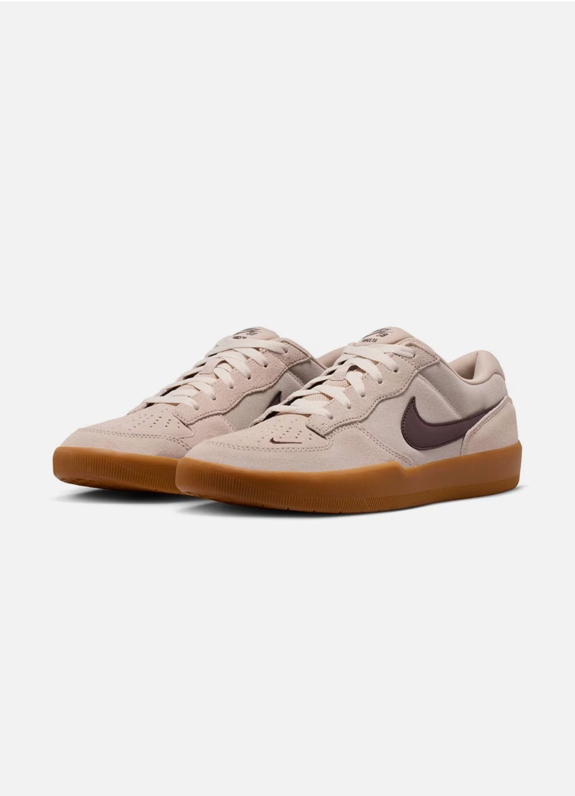 A pair of Nike low-top sneakers in a light beige suede and leather combination, featuring a dark brown Swoosh on the side and a gum brown sole, set against a plain light gray background.