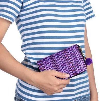 Person holding a purple clutch with a pattern, wearing a blue and white striped shirt.