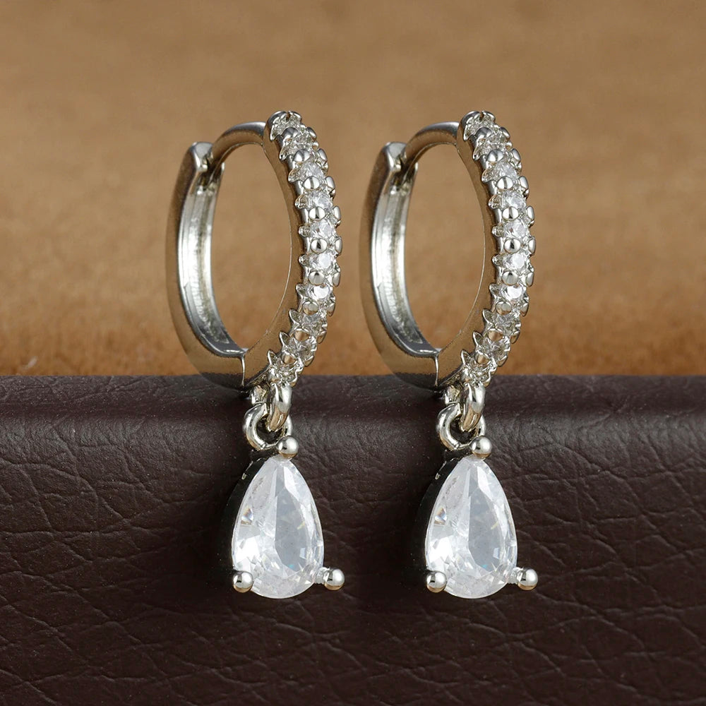 Silver hoop earrings with teardrop-shaped gemstones on a brown surface