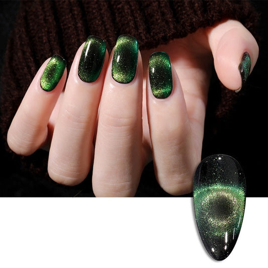 A hand with long oval nails painted in a metallic green magnetic cat-eye manicure, shown against a dark knit sweater, with a separate nail swatch inset at the bottom right displaying the same green glittery magnetic effect.