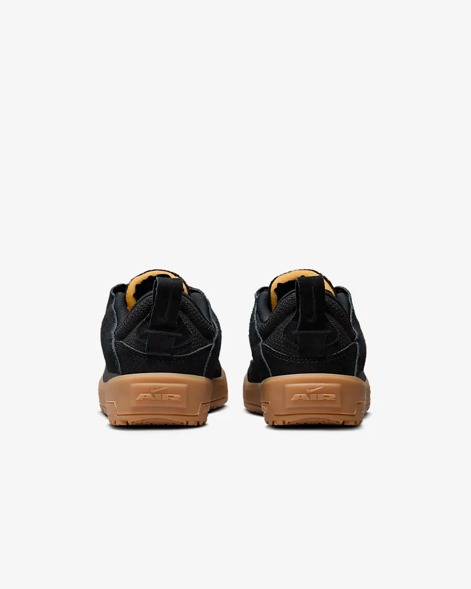 A pair of black low-top sneakers shown from the back, featuring tan rubber soles and a small yellow accent on the tongue lining, set against a plain light gray background. Nike SB Day One - Youth - FN4210-001