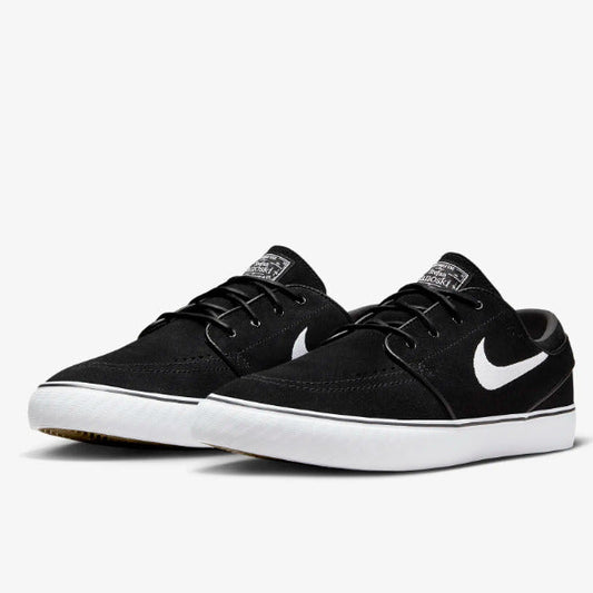 A pair of Nike low-top skate shoes in black canvas with a white Swoosh and white rubber sole, shown against a light gray background. Nike SB Janoski Black White