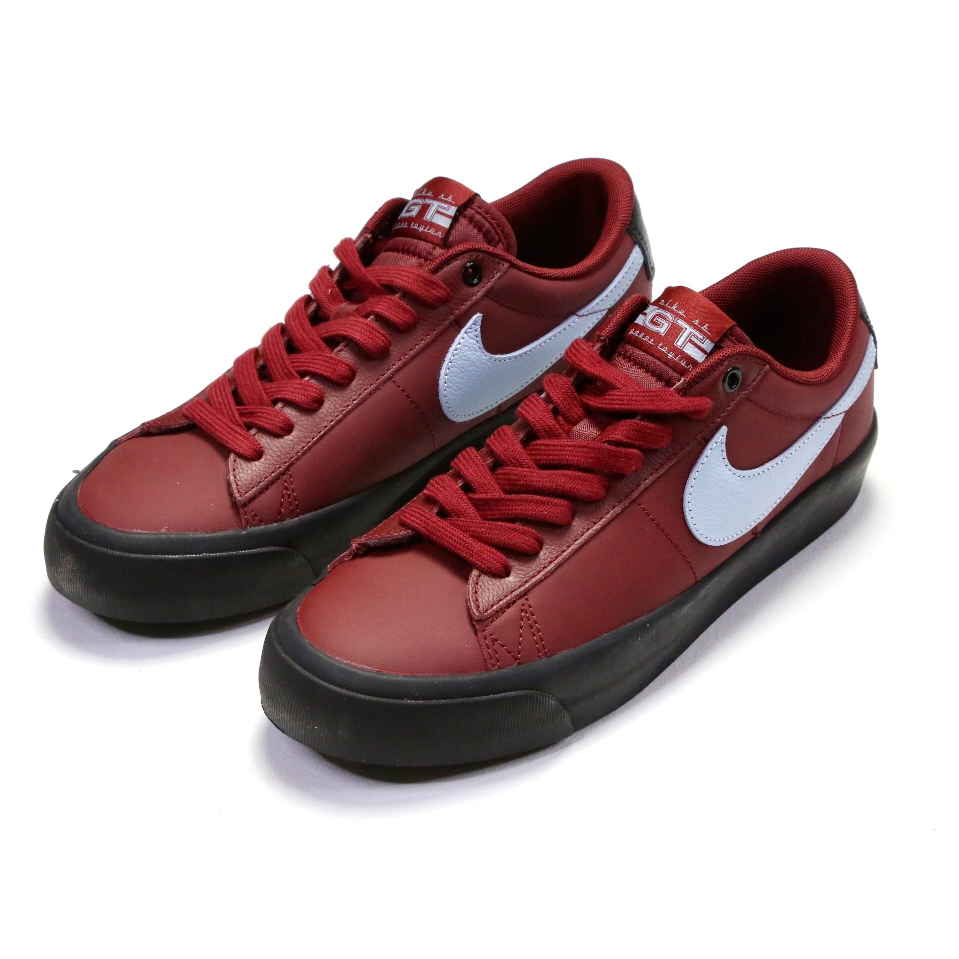 A pair of Nike low-top sneakers in a dark red colorway, featuring a white Swoosh logo and black soles, photographed on a clean white background. Nike SB Blazer Low Pro GT DV1226-600