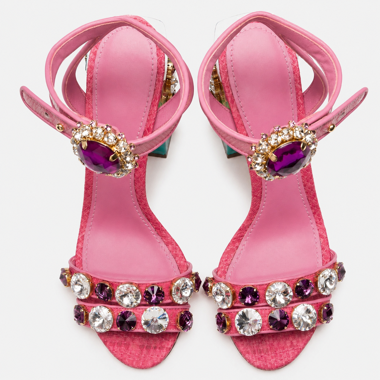 A pair of pink high-heeled sandals decorated with large purple and clear rhinestones on the straps and heels, shown against a plain white background.