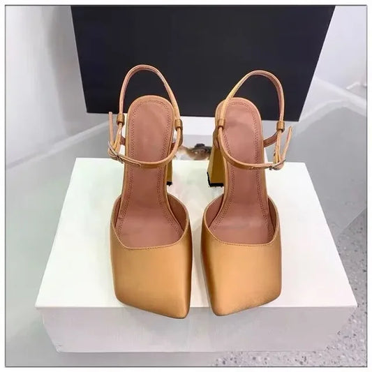Women's metallic gold square-toe slingback block heel sandals displayed on a white pedestal with a black and white backdrop. Square tip heels.