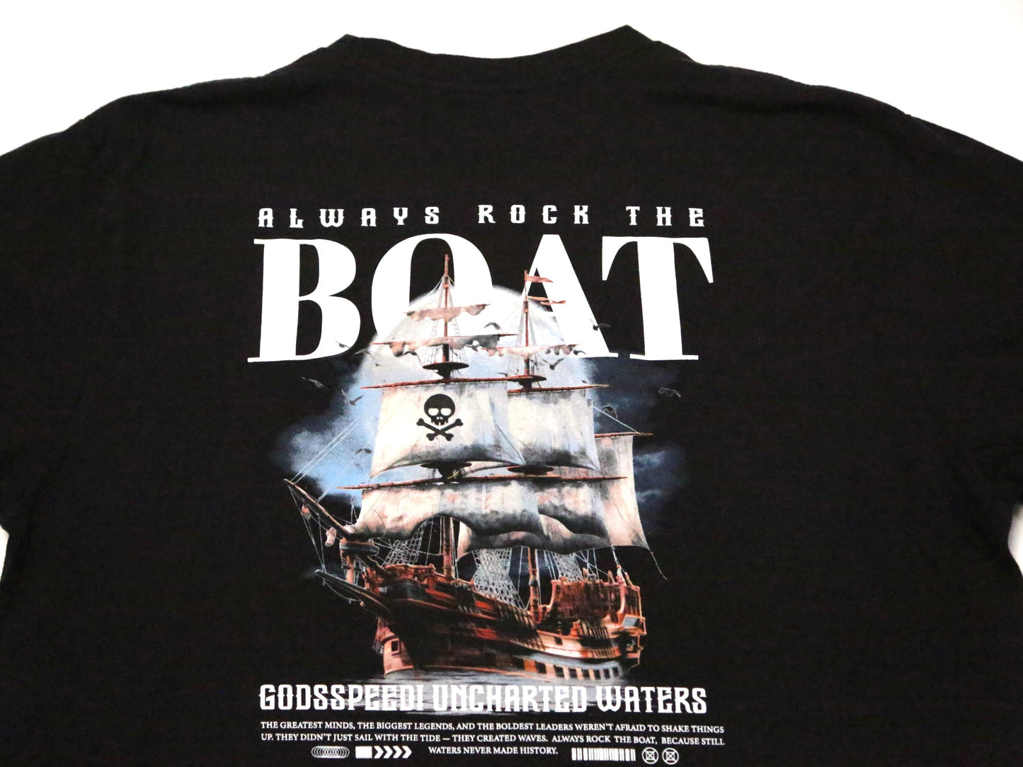 A black t-shirt featuring a large graphic print of a pirate ship with a skull and crossbones on the main sail, accompanied by the text 'ALWAYS ROCK THE BOAT' and 'GODSPEED UNCHARTED WATERS'.