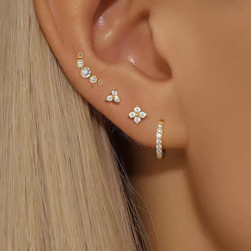 Close-up of an ear wearing multiple gold and diamond earrings against a neutral background