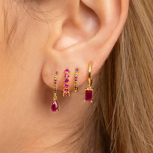 Close-up of an ear wearing gold hoop earrings with gemstones.