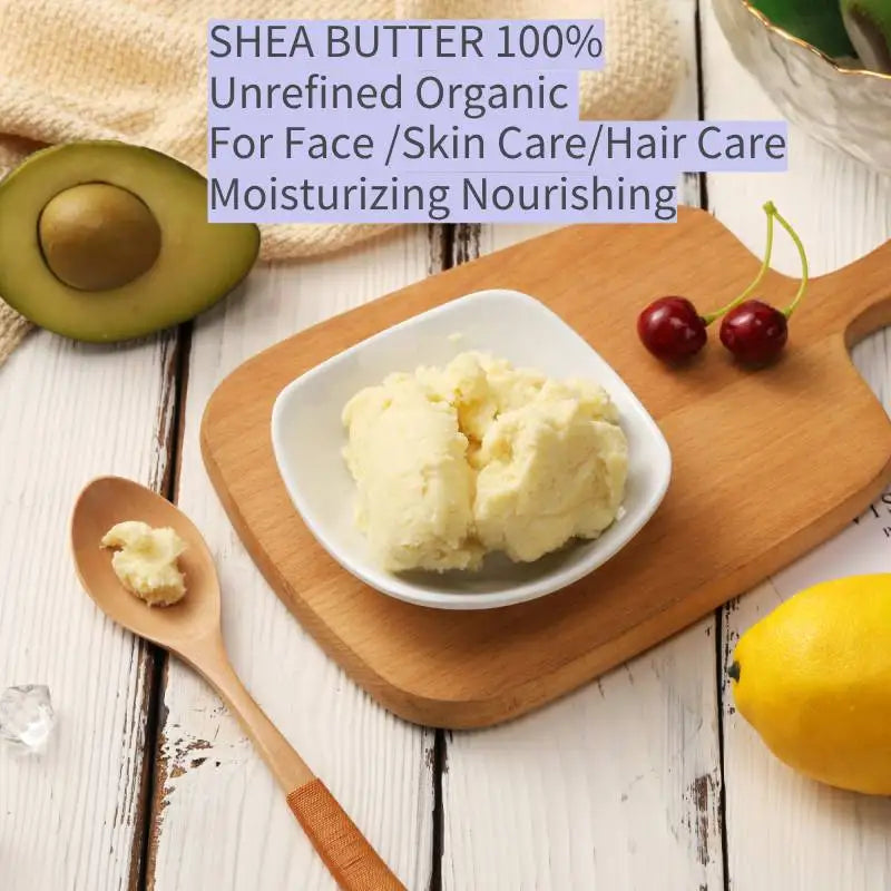 Shea butter in a white bowl on a wooden cutting board with an avocado, cherry, and lemon on a light wood background.