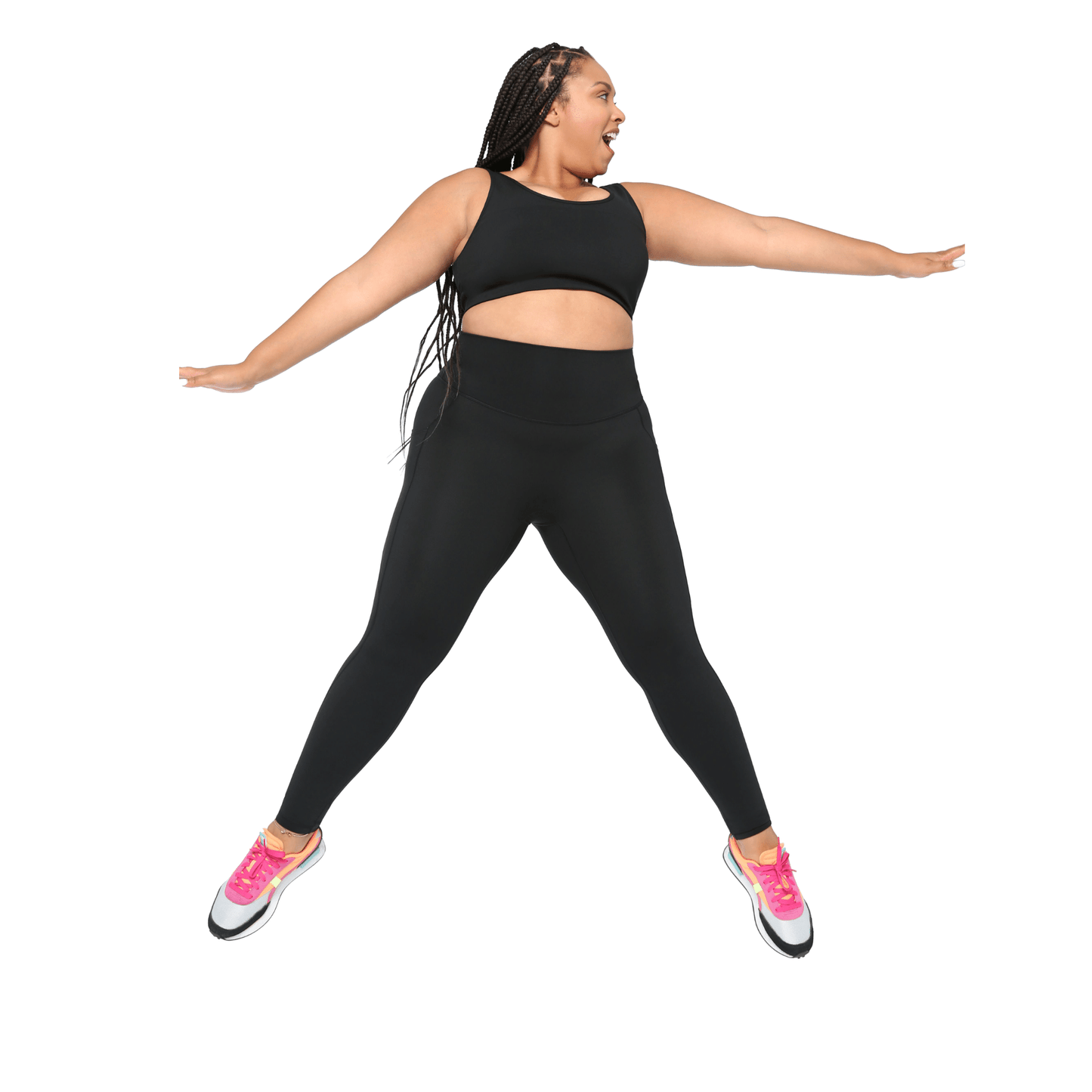 Plus size woman modeling a black high-support sports bra and matching high-waisted leggings with bright pink sneakers, active fitness pose on white background.