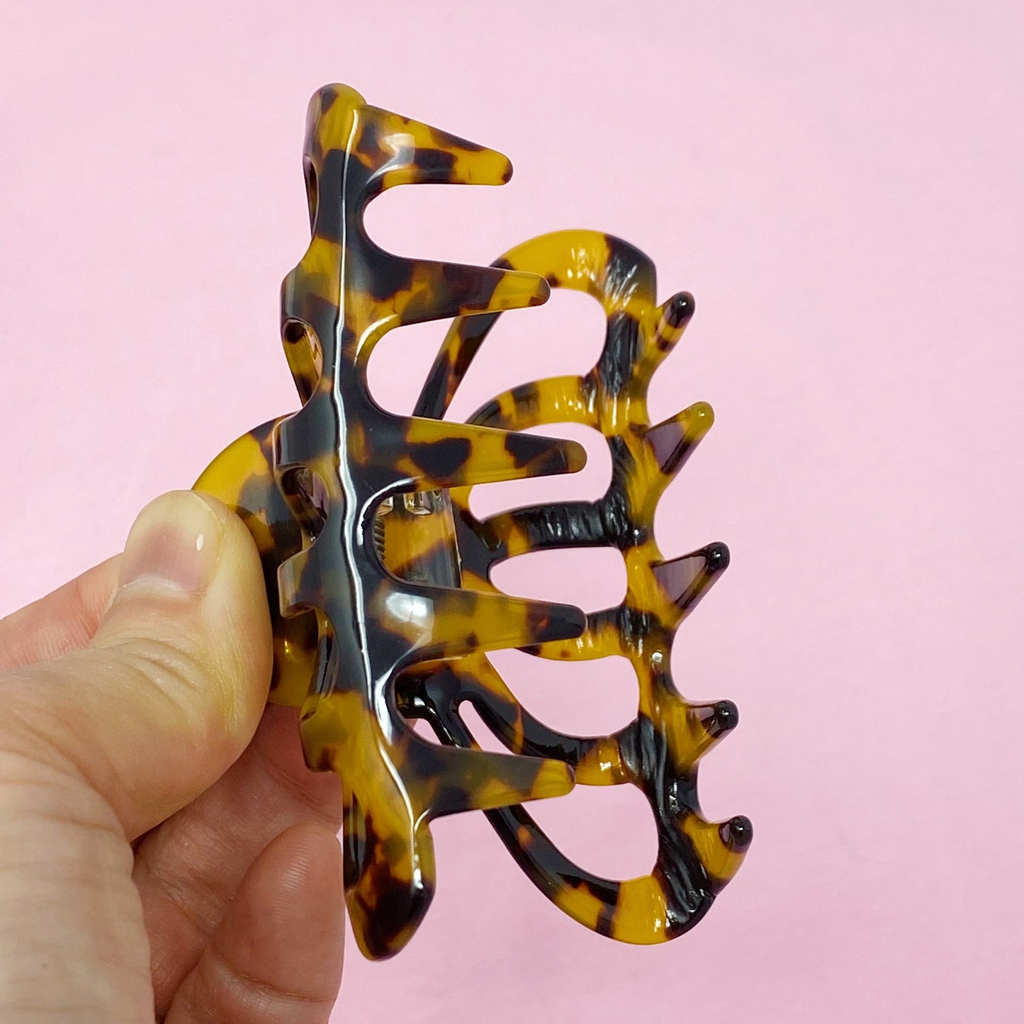 Tortoiseshell patterned hair clip held by a hand against a pink background
