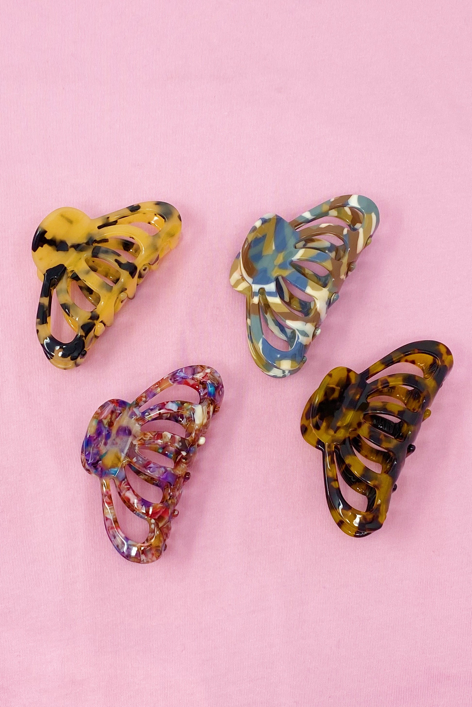 Four colorful butterfly-shaped hair clips on a pink background
