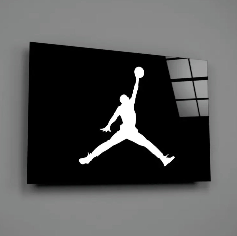 Black glass wall art with a white silhouette of a person jumping and holding a basketball on a gray background. Michael Jordan Air Jordan Glass Wall Art piece