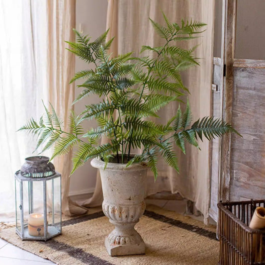 Potted fern plant in a decorative urn with a lantern and basket in a room setting.