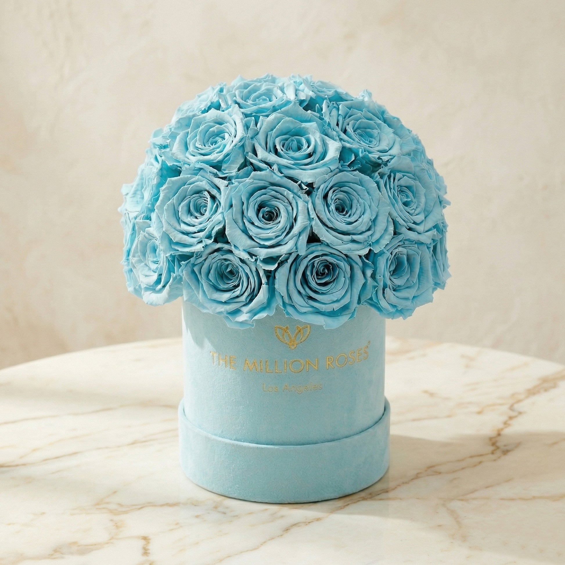 Blue roses in a round box with 'The Million Roses' logo on a marble surface. Essence Mint Green Suede Superdome Box | Turquoise Roses