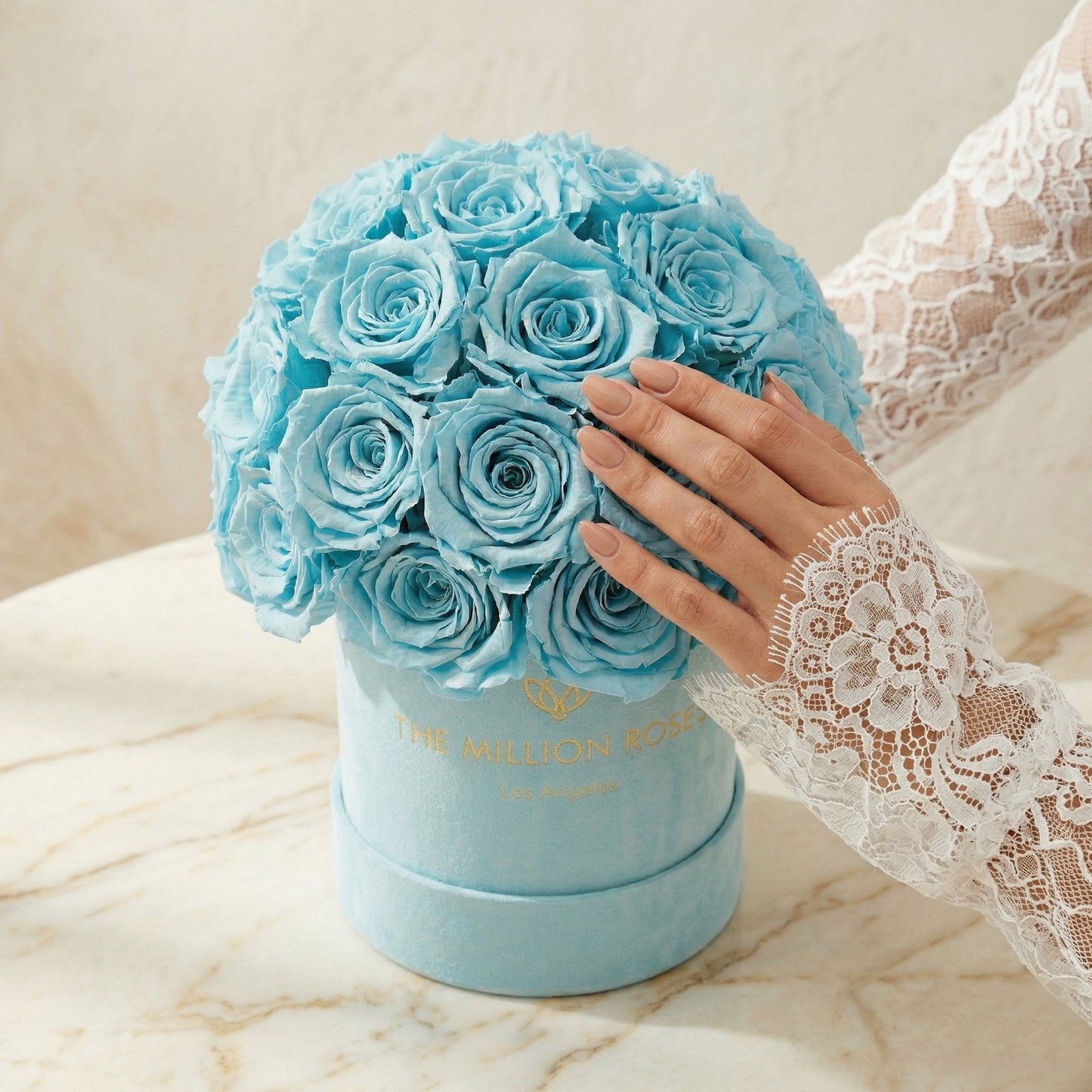 Blue bouquet of roses in a box held by a hand with lace sleeve on a marble. Essence Mint Green Suede Superdome Box | Turquoise Rosessurface