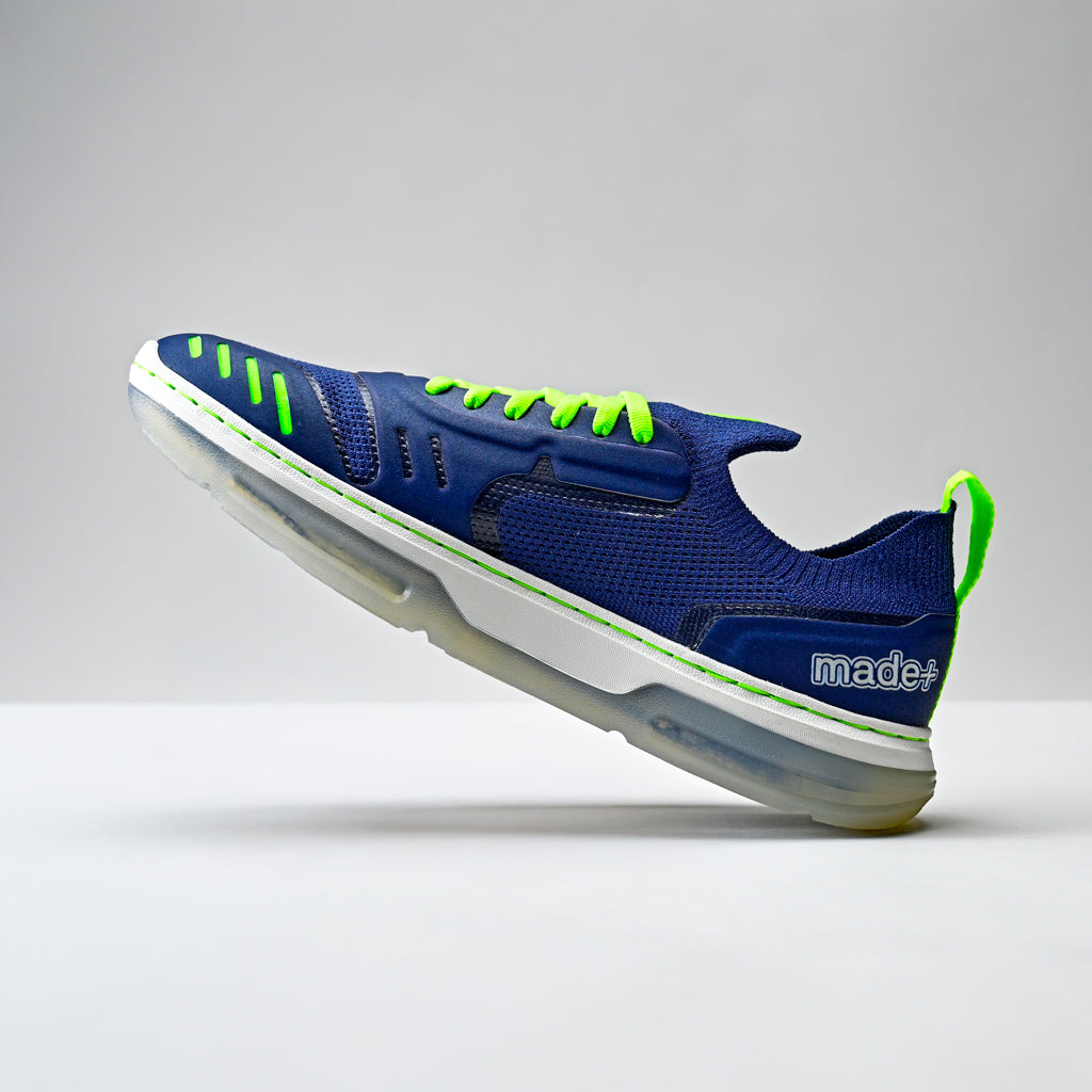Blue running shoe with green accents on a gray background